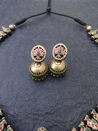Pair of gold earrings with green and red stones on a textured dark surface